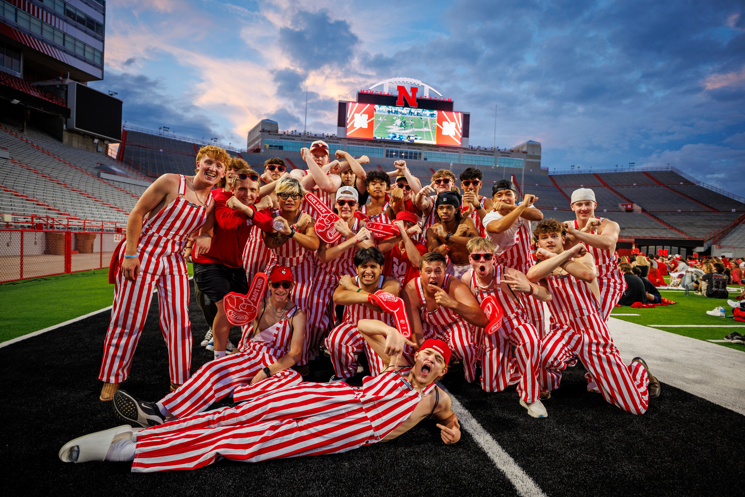 a photo of students at the memorial stadium watch party dressed in red and white striped overalls cheering on the huskers