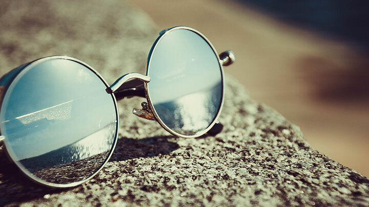 Sunglasses rest on a surface outside, reflecting a sunny sky.
