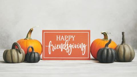 Sign with cursive text that reads "Happy Friendsgiving" surrounded by pumpkins