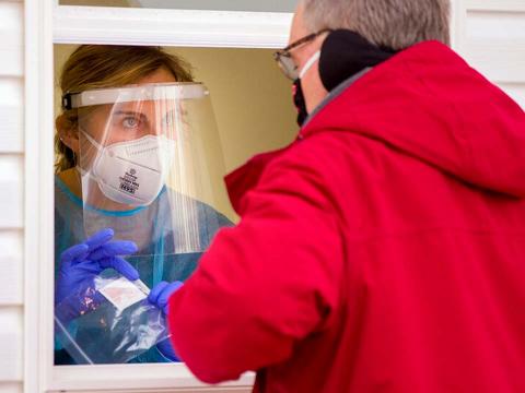 Man in red coat stands outside saliva testing pod