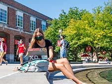 Student wearing mask studies in front of Broyhill Fountain