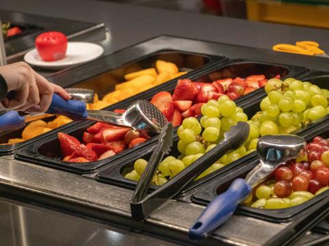 A student scoops some cut strawberries from the serving line