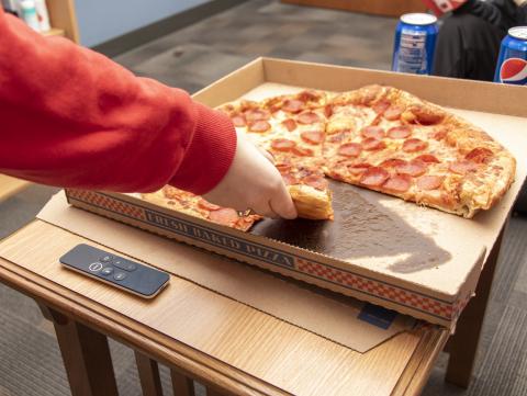 A student grabs a slice of pizza from a pizza box.