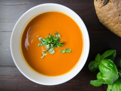 Tomato soup with basil and rye bread on a table.